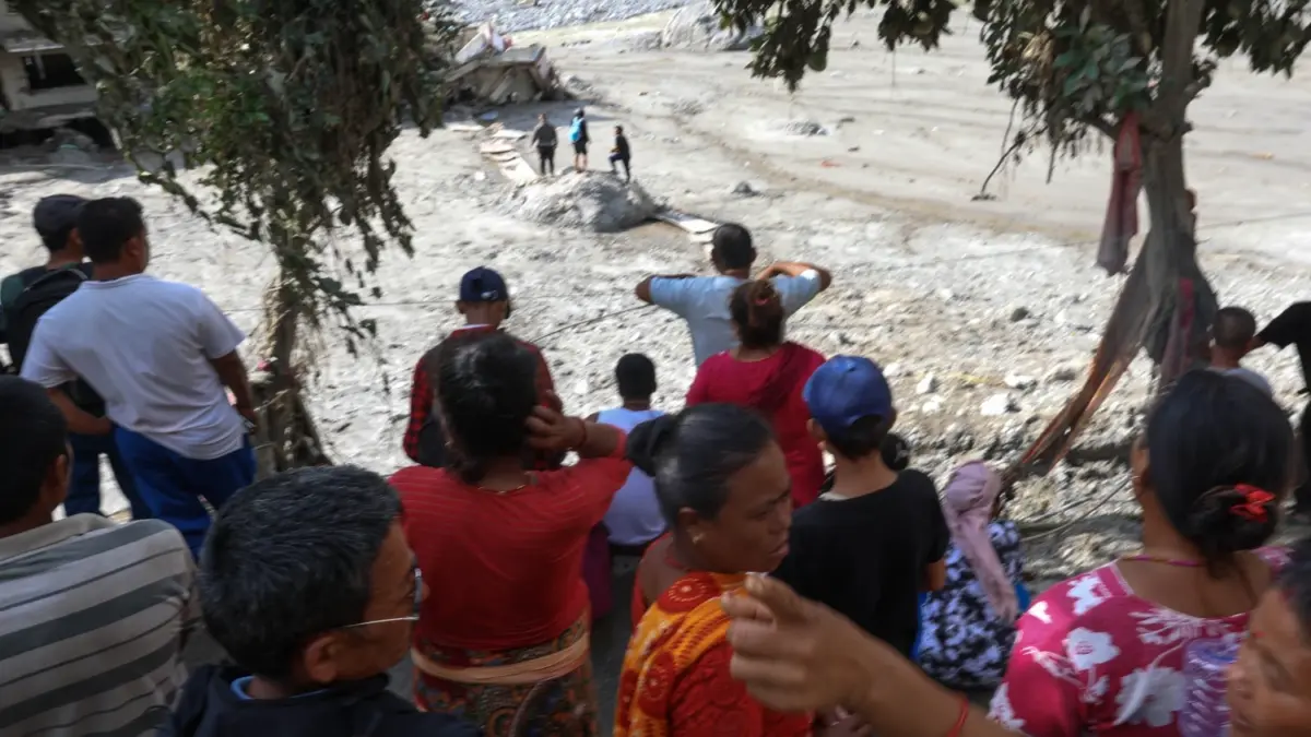 A ground of people on higher ground look on at the land covered in mud. Photo by Suman Nepali of Nepali Times. Used with permission.